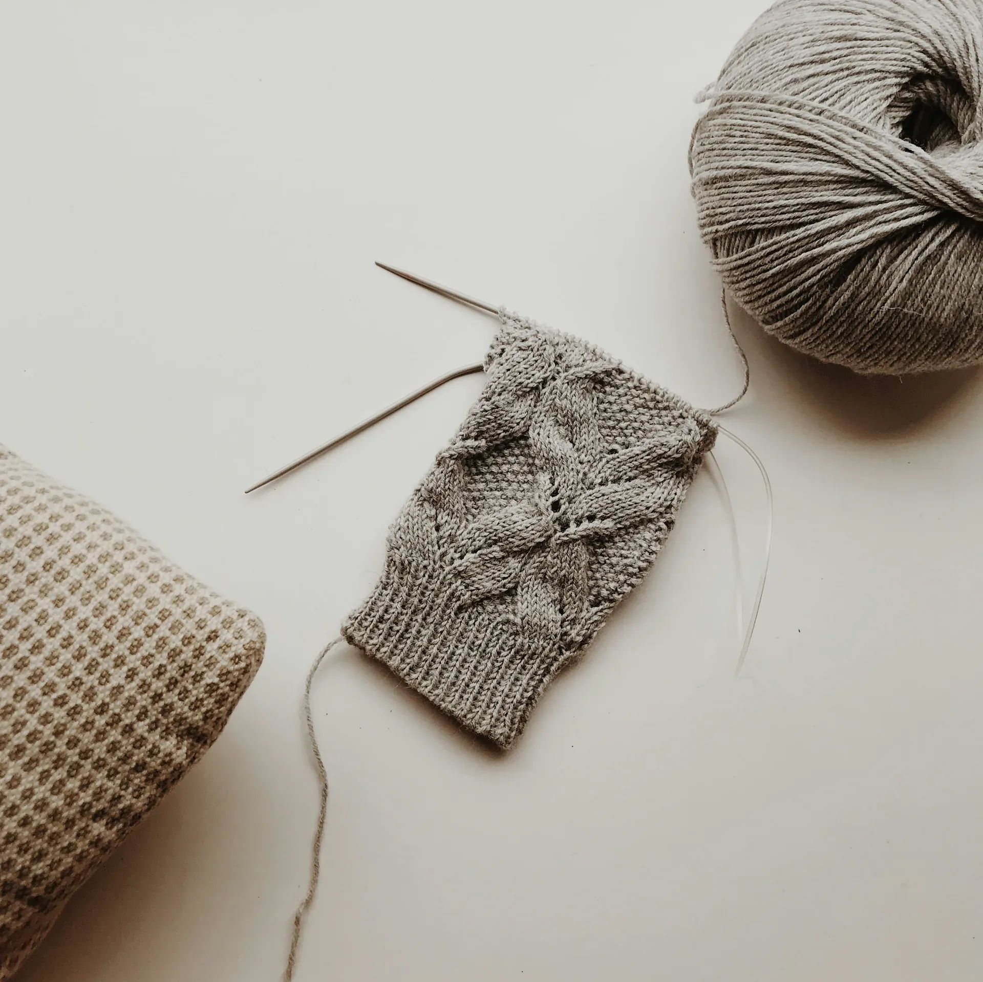 Grey lace knitting in progress with a ball of grey yarn and a knitted cushion