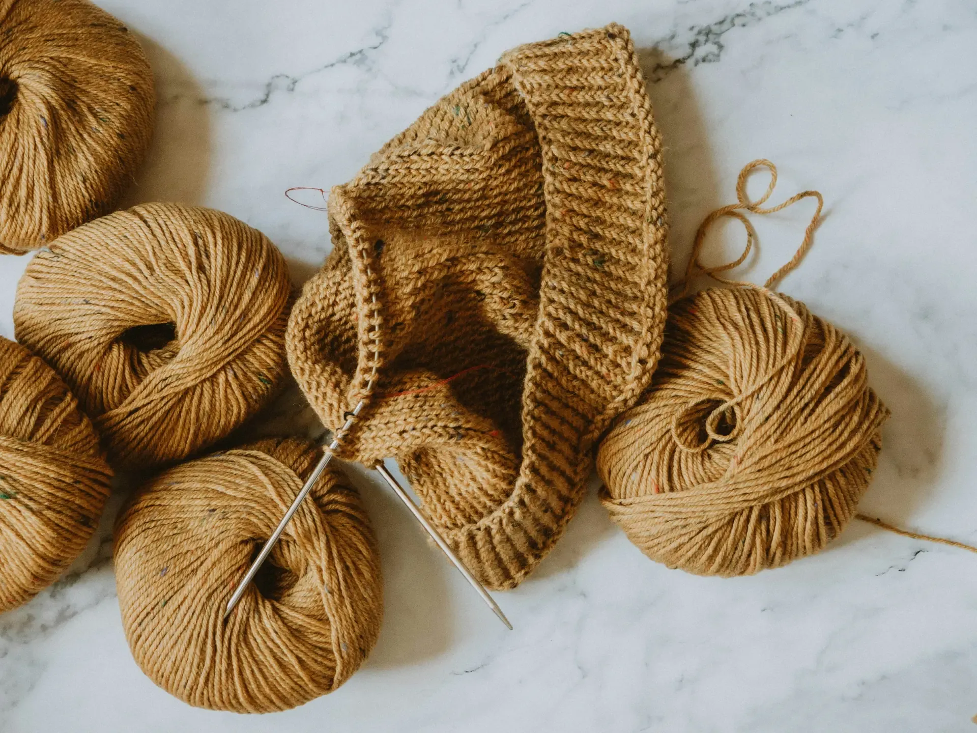 Caramel yarn balls and knitting in progress on a marble surface
