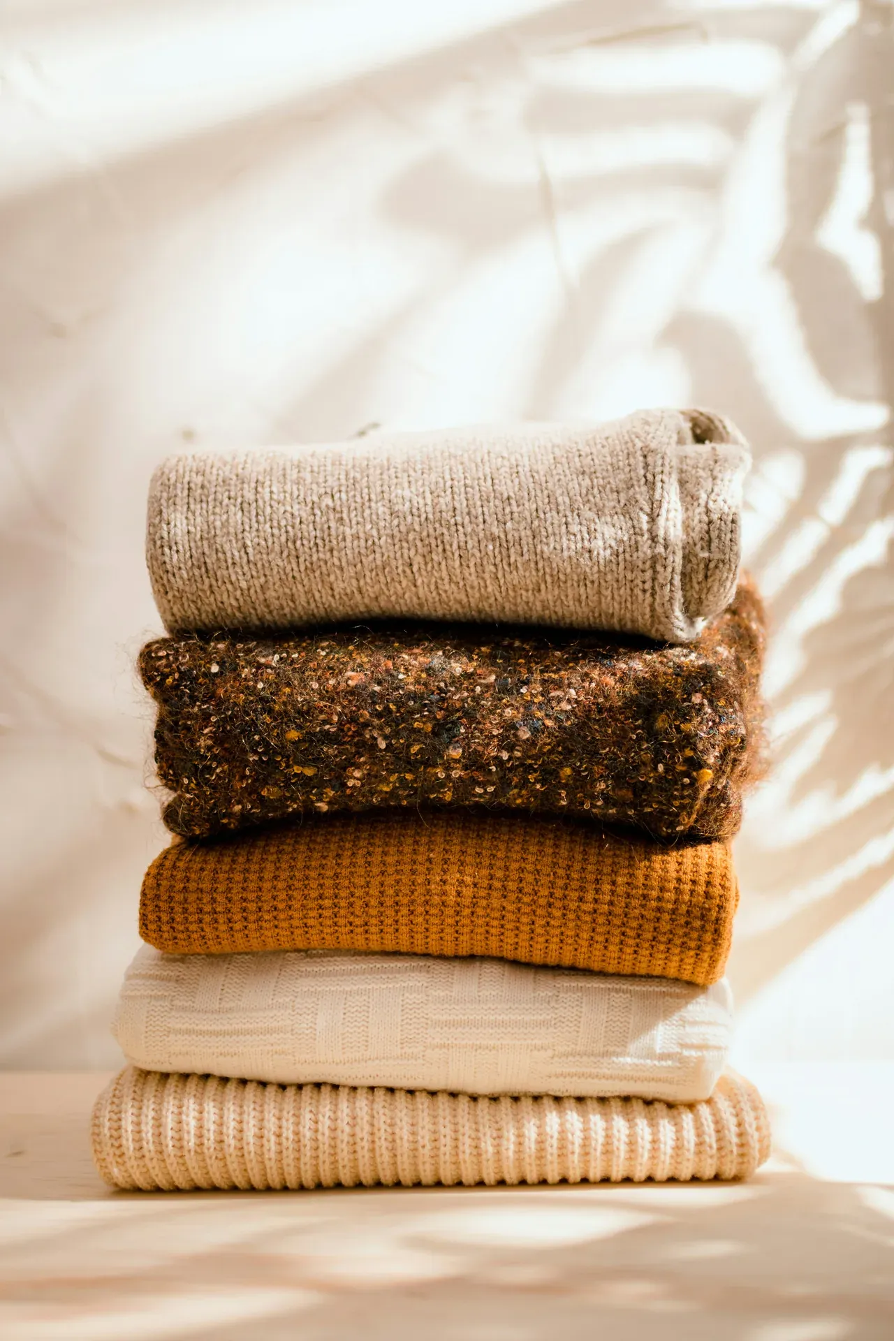 Stack of folded knitted sweaters in warm neutral tones